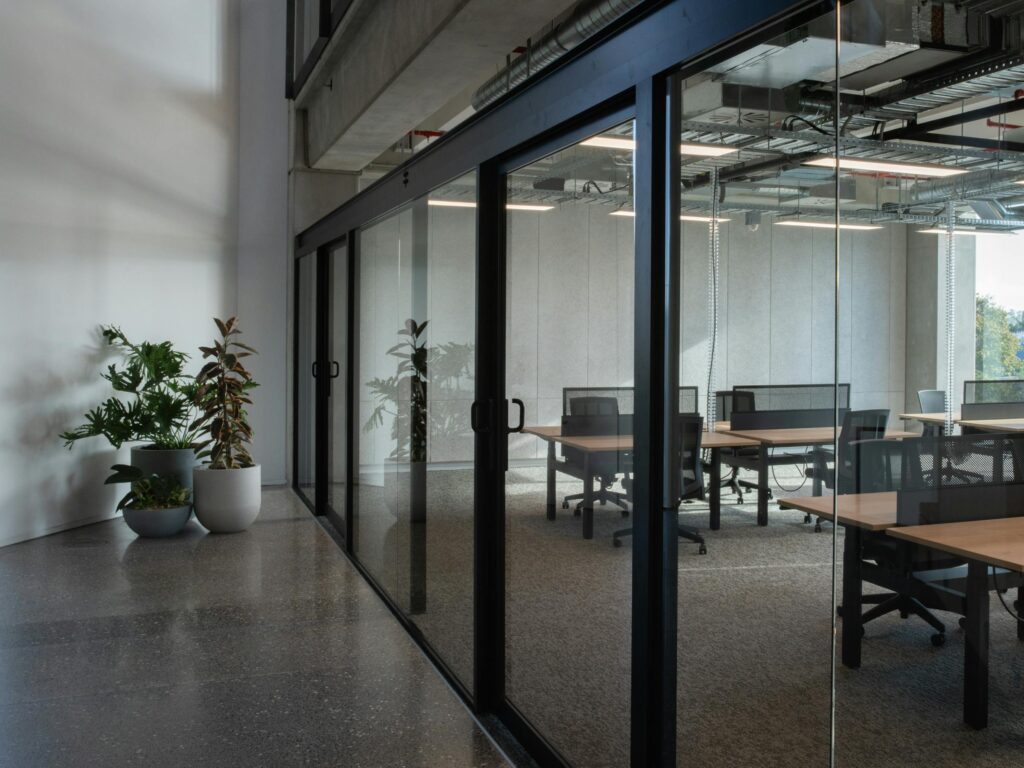 Glass-partitioned office space with hot-desks and plants in a polished concrete corridor