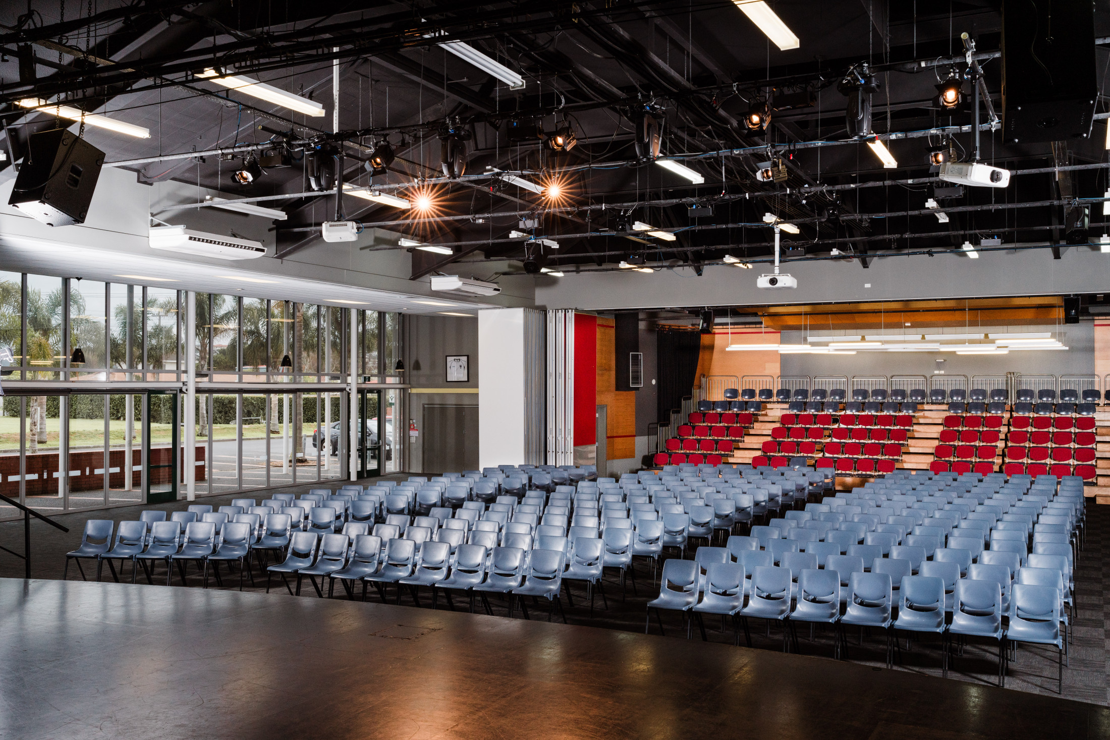 Multi-purpose hall with stage, tiered seating, and exposed black ceiling grid with stage lighting