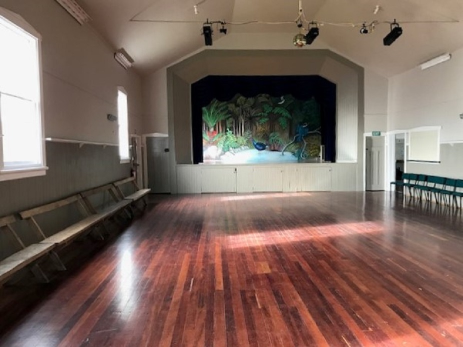 Hall interior with polished timber floor, raised platform with painted forest mural backdrop, and stage lighting