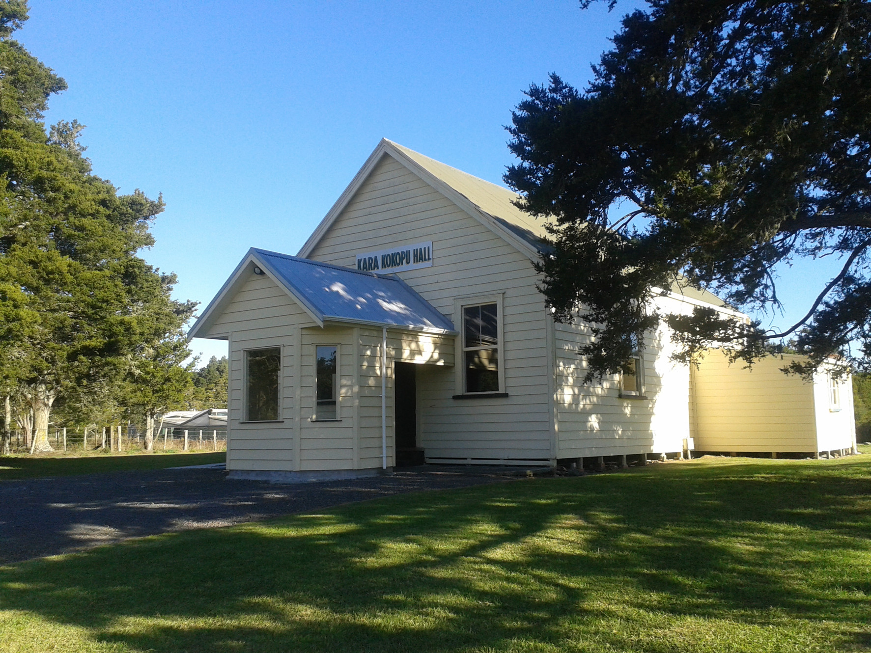 Small white timber hall with metal roof and signage on grassed section