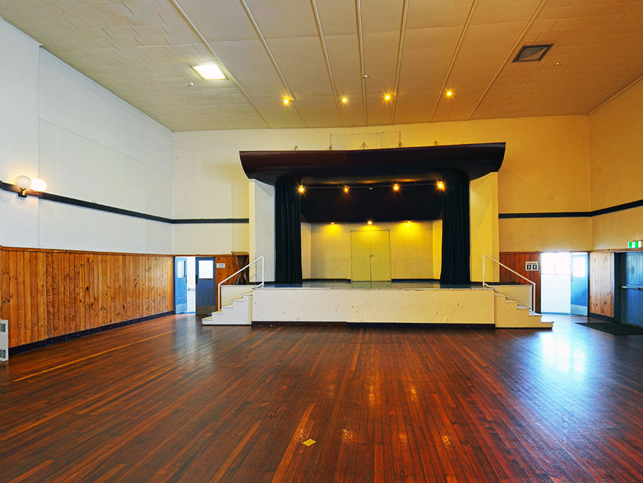 Timber-floored hall with raised platform, dark curtains, timber wall panelling and overhead spotlights