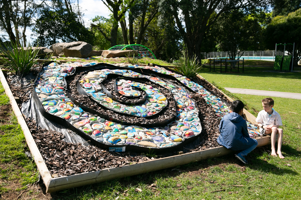 Children beside a painted-stone spiral garden feature in school grounds
