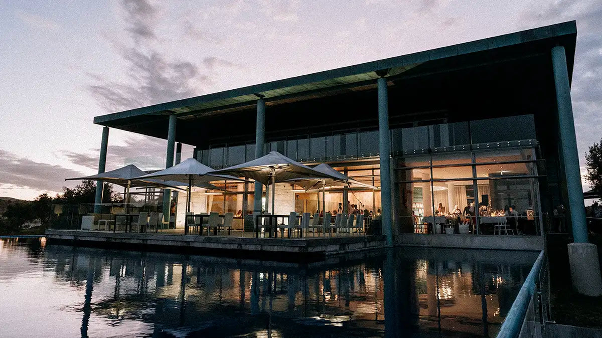 Winery building at dusk reflected in an infinity pool with lit terrace umbrellas