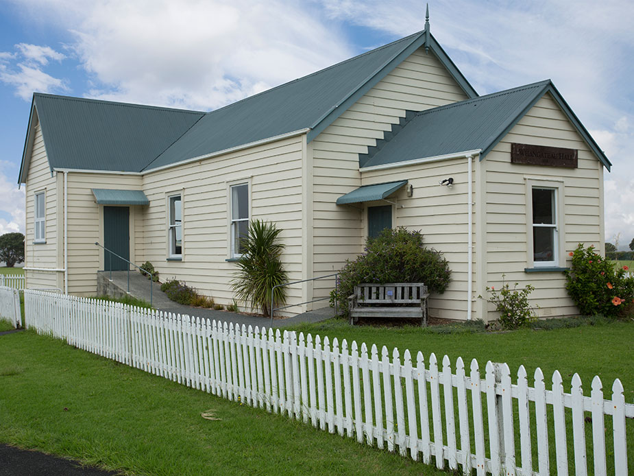 Cream weatherboard hall with teal roof and picket fence in open rural setting
