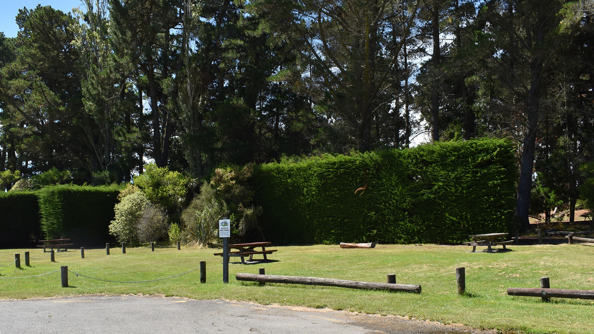Sheltered picnic area with tables, hedging and tall trees