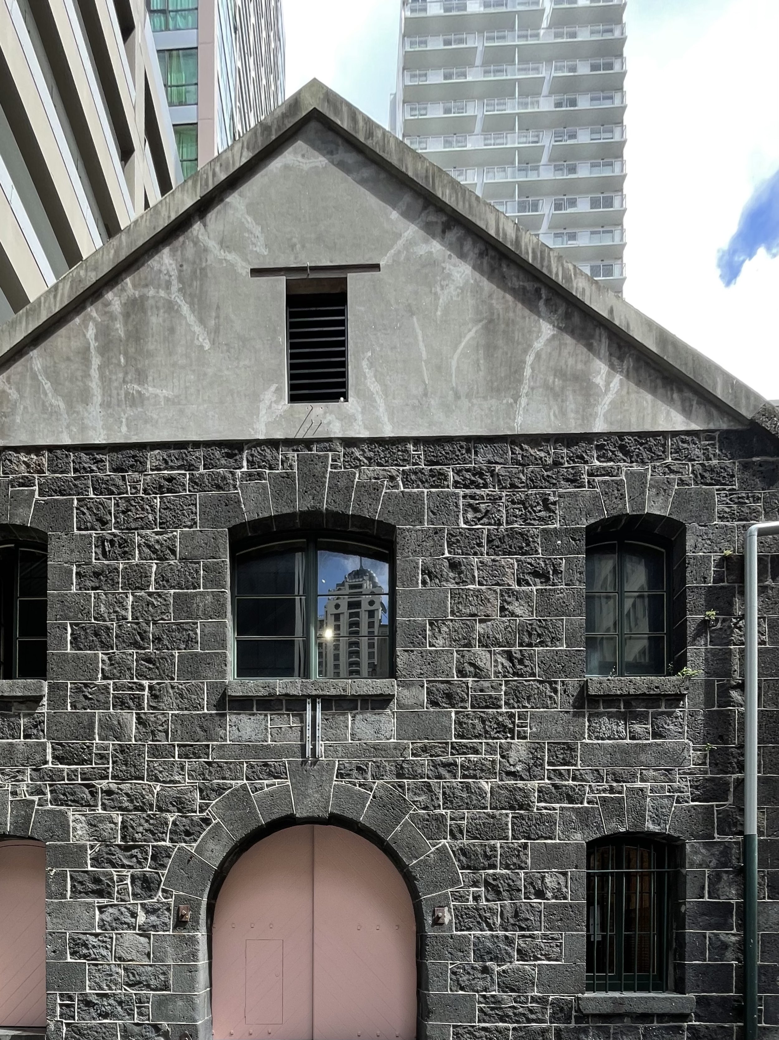 Dark basalt stone warehouse exterior with arched entry and gabled roofline, flanked by city towers