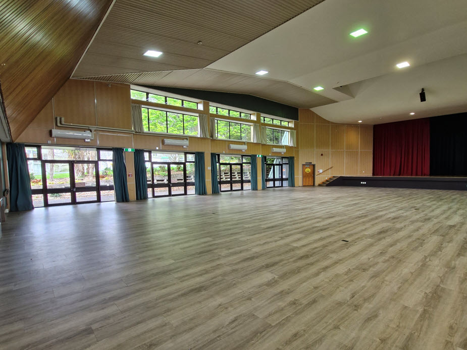 Large function hall with timber ceiling, raised platform and red curtains
