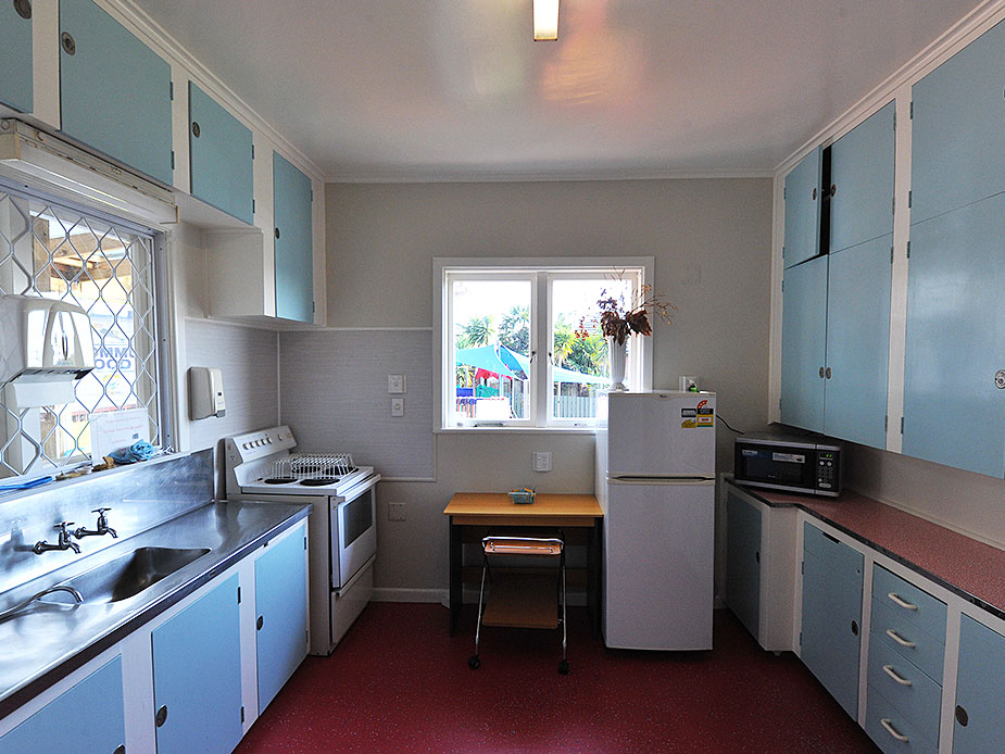 Older kitchen with blue cabinetry, stainless bench, fridge and small table