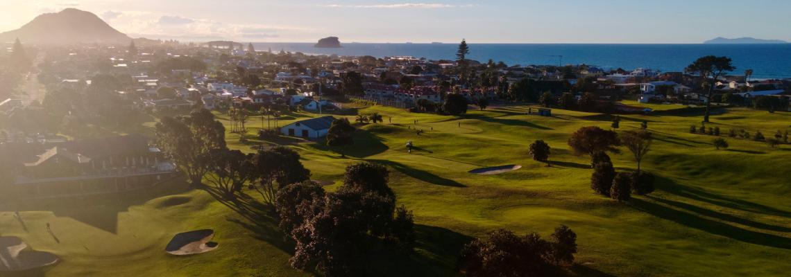 Aerial view of golf course fairways with coastal town and sea beyond