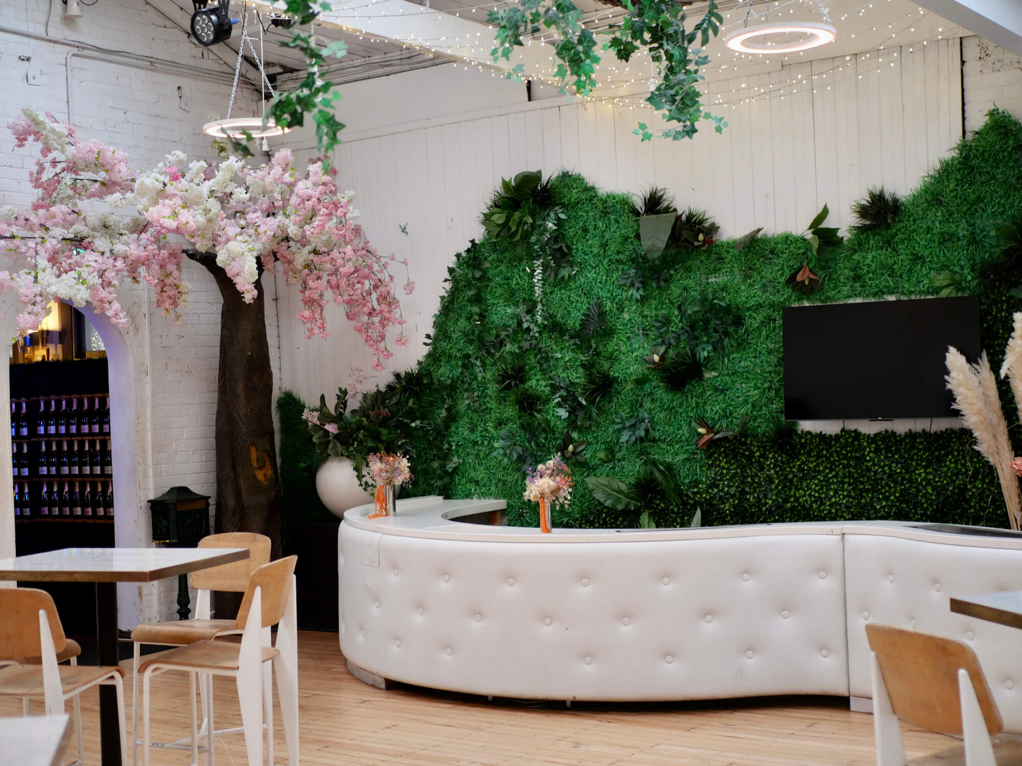 Bright white room with green foliage wall, white curved bar, and flowering tree installation