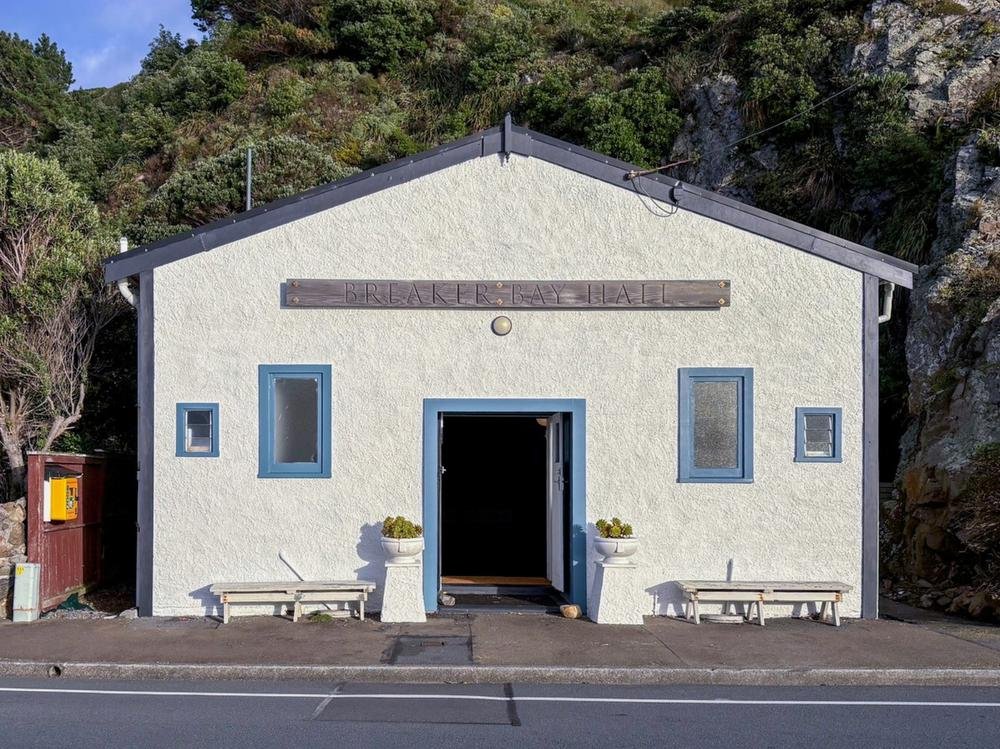 White rendered hall with blue trim and timber sign above entrance
