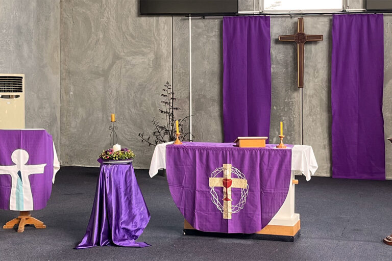 Church sanctuary interior with altar table draped in purple, wooden cross, and candles