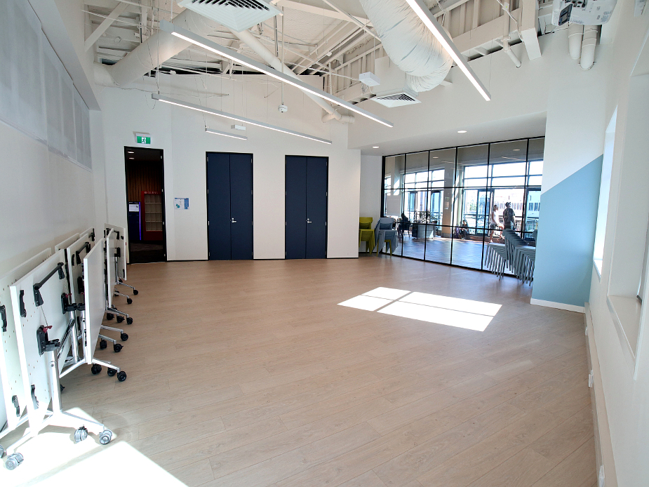 Open activity room with timber floor, folded tables, and glass partitions