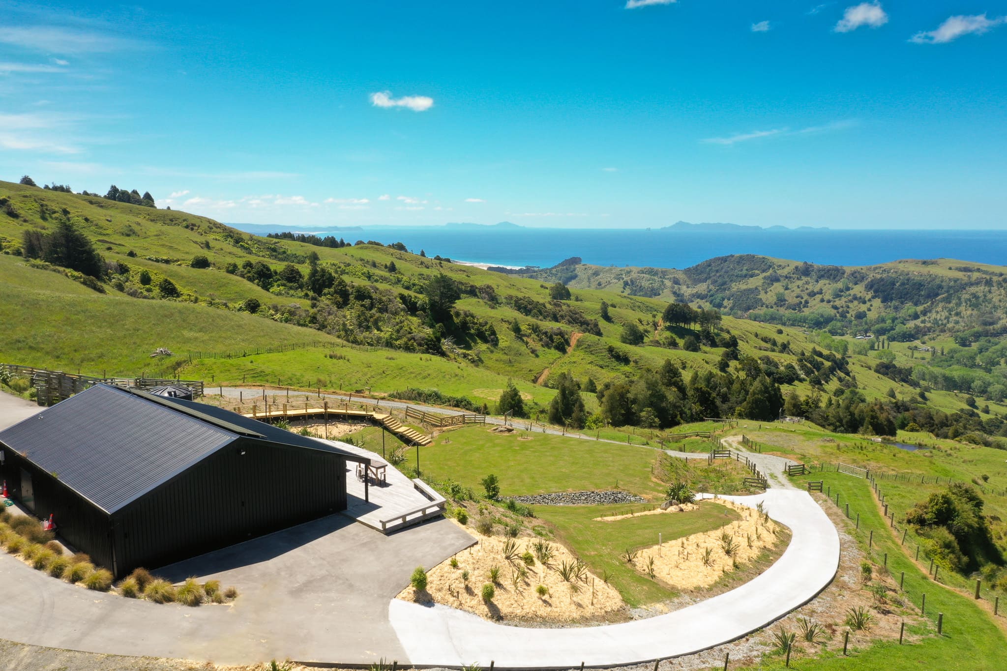 Aerial view of black barn venue beside a curved driveway with panoramic rural and coastal views