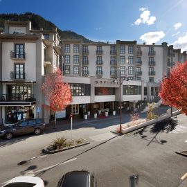 Pale multi-storey hotel building on a street corner with trees and mountains behind