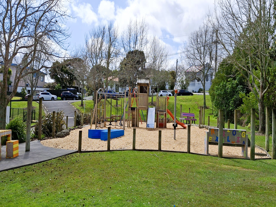 Playground equipment on bark chip surface with log post boundary markers and surrounding lawn