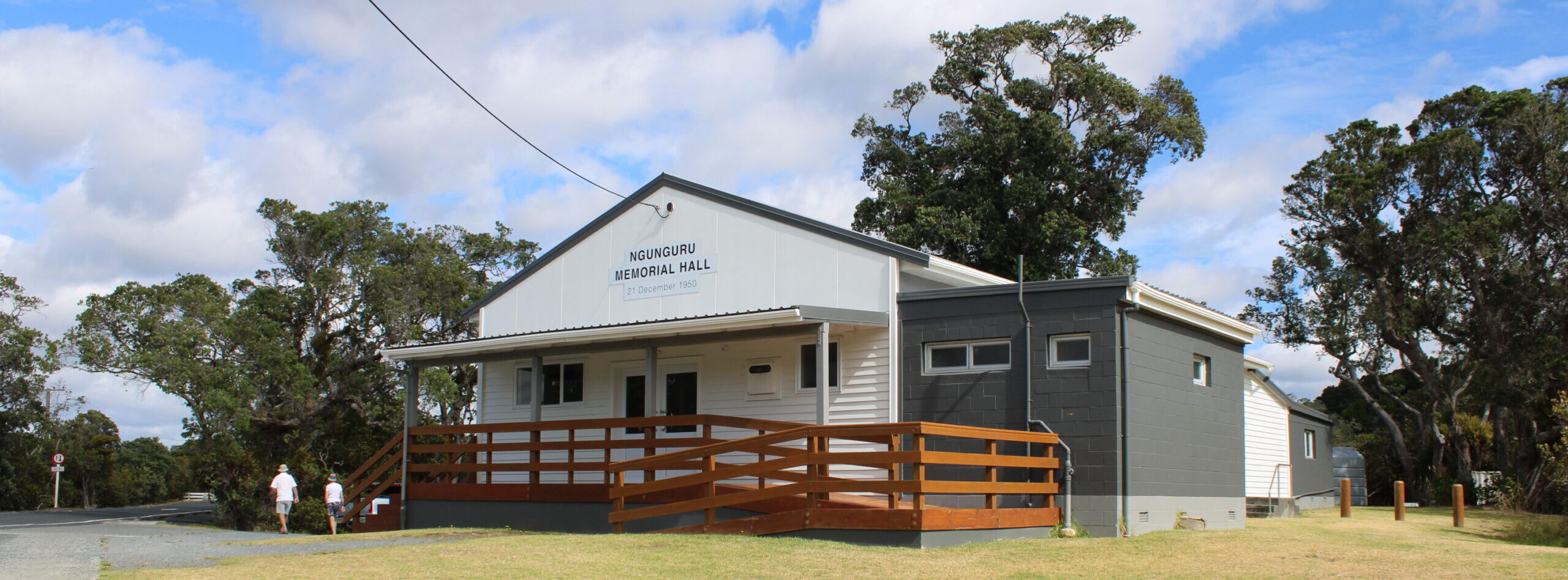 Small white memorial hall with timber deck, ramp and dark addition at rear