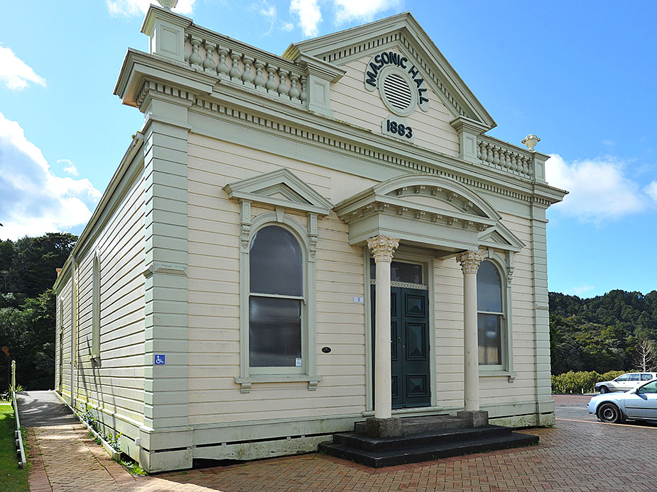Cream weatherboard hall with classical columns and arched doorway, side view on brick paving