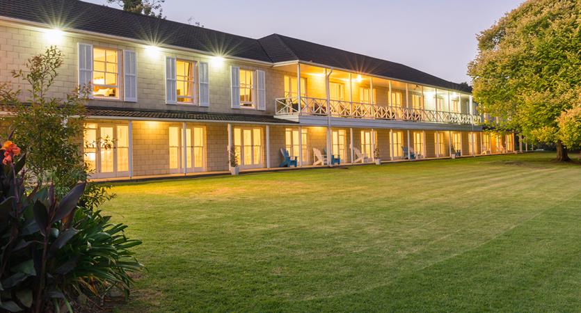 Two-storey hotel building at dusk with lawn, verandah and warm interior lighting
