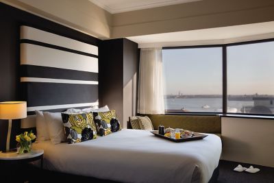Hotel room with monochrome striped headboard, patterned cushions, and large harbour-view window