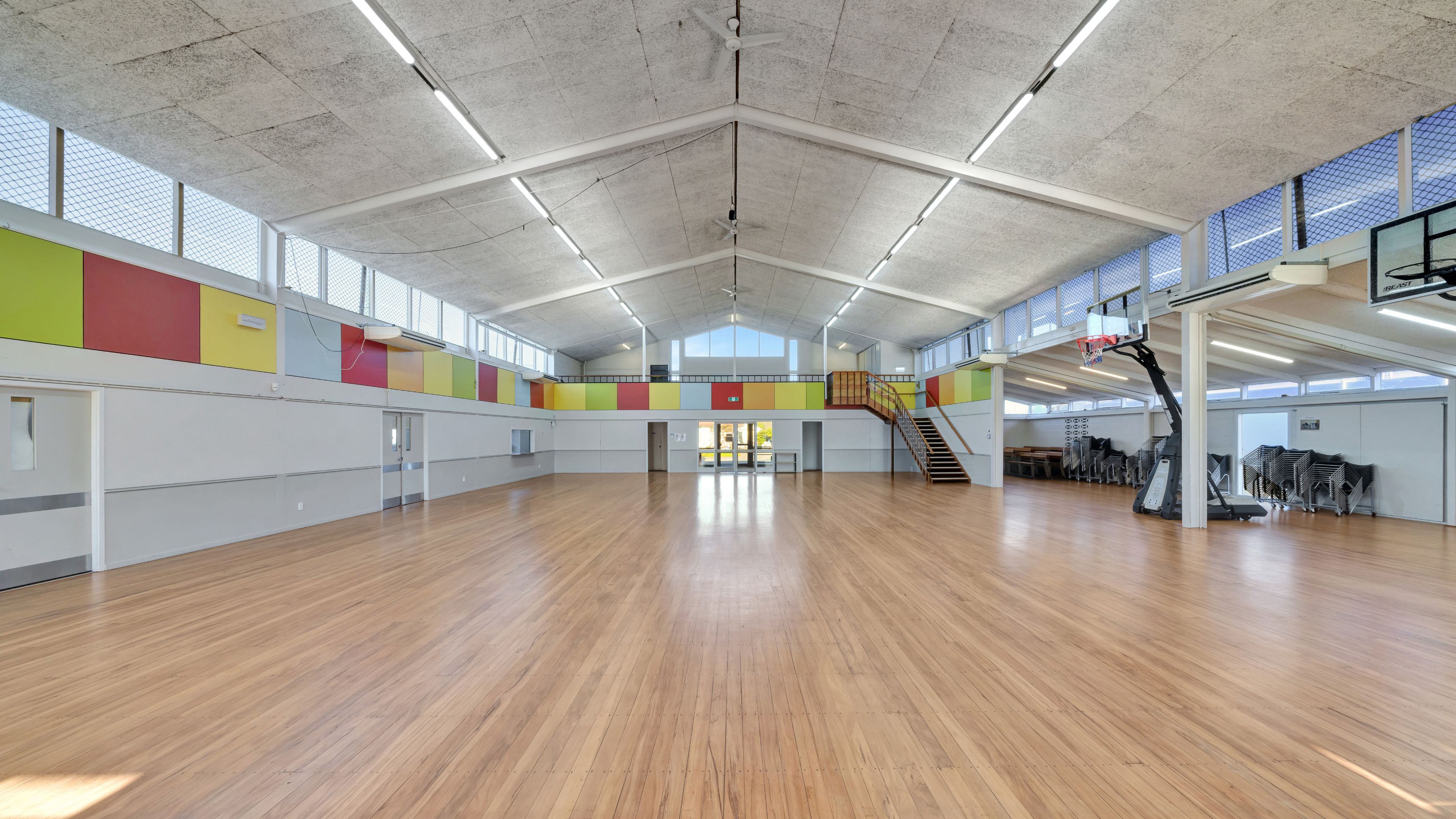 Large sports hall with timber floor, vaulted ceiling, colourful wall panels and basketball hoop