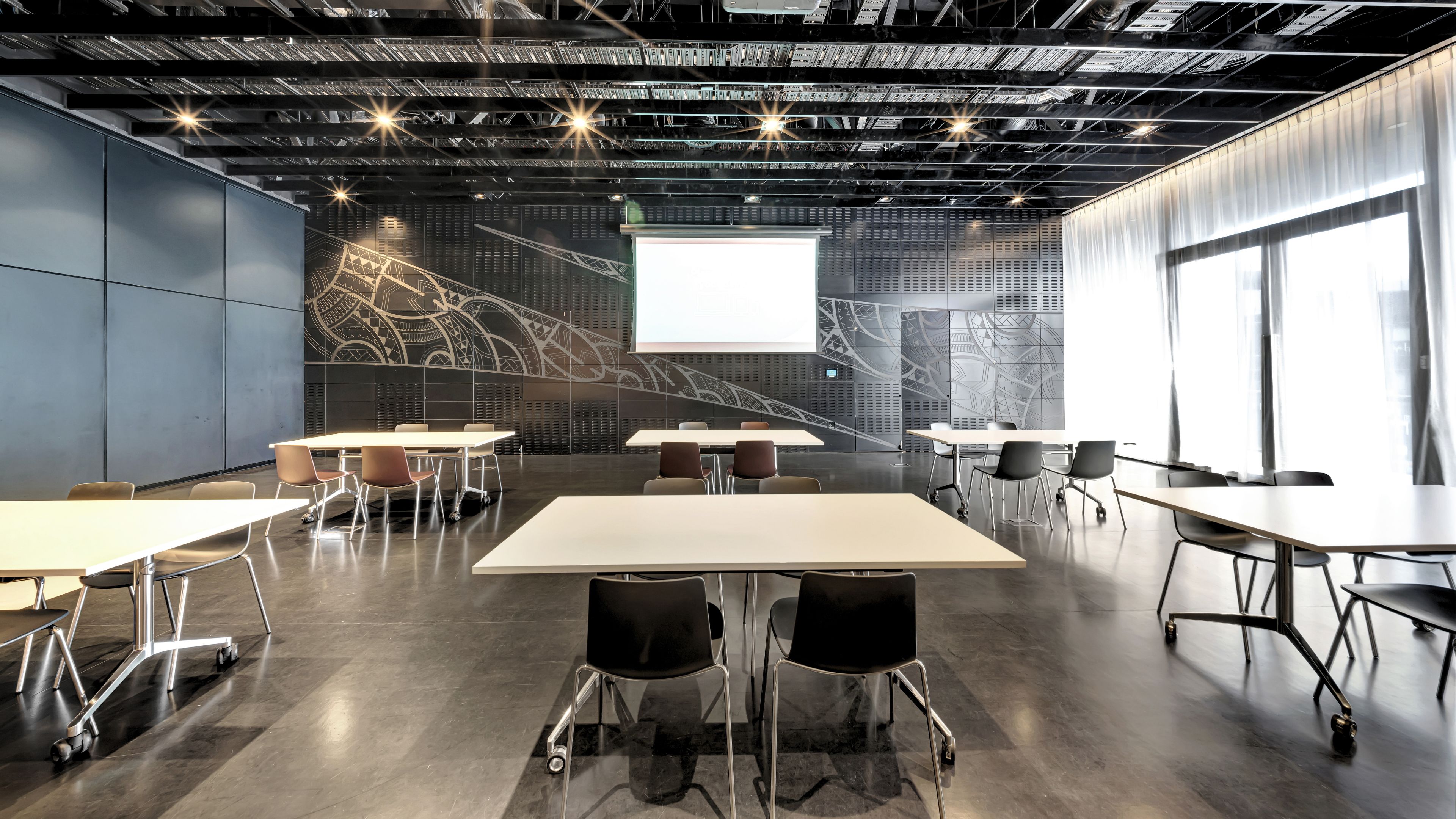 Meeting room with tables and chairs, dark feature wall with Maori-inspired mural