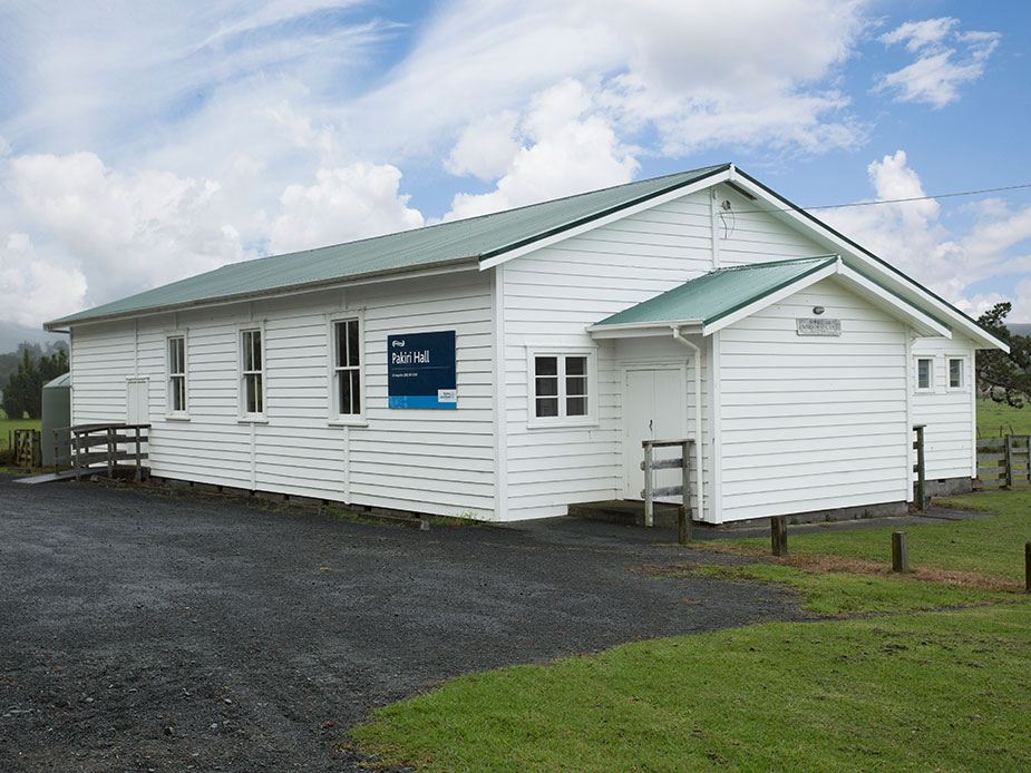 White weatherboard hall with green metal roof, gravel car park, and paddock setting