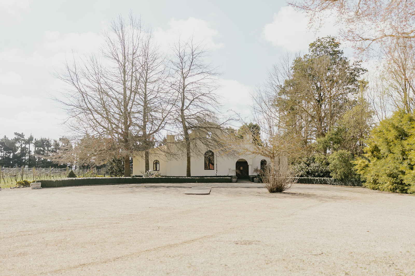 White rendered venue building with arched windows surrounded by bare deciduous trees and vines