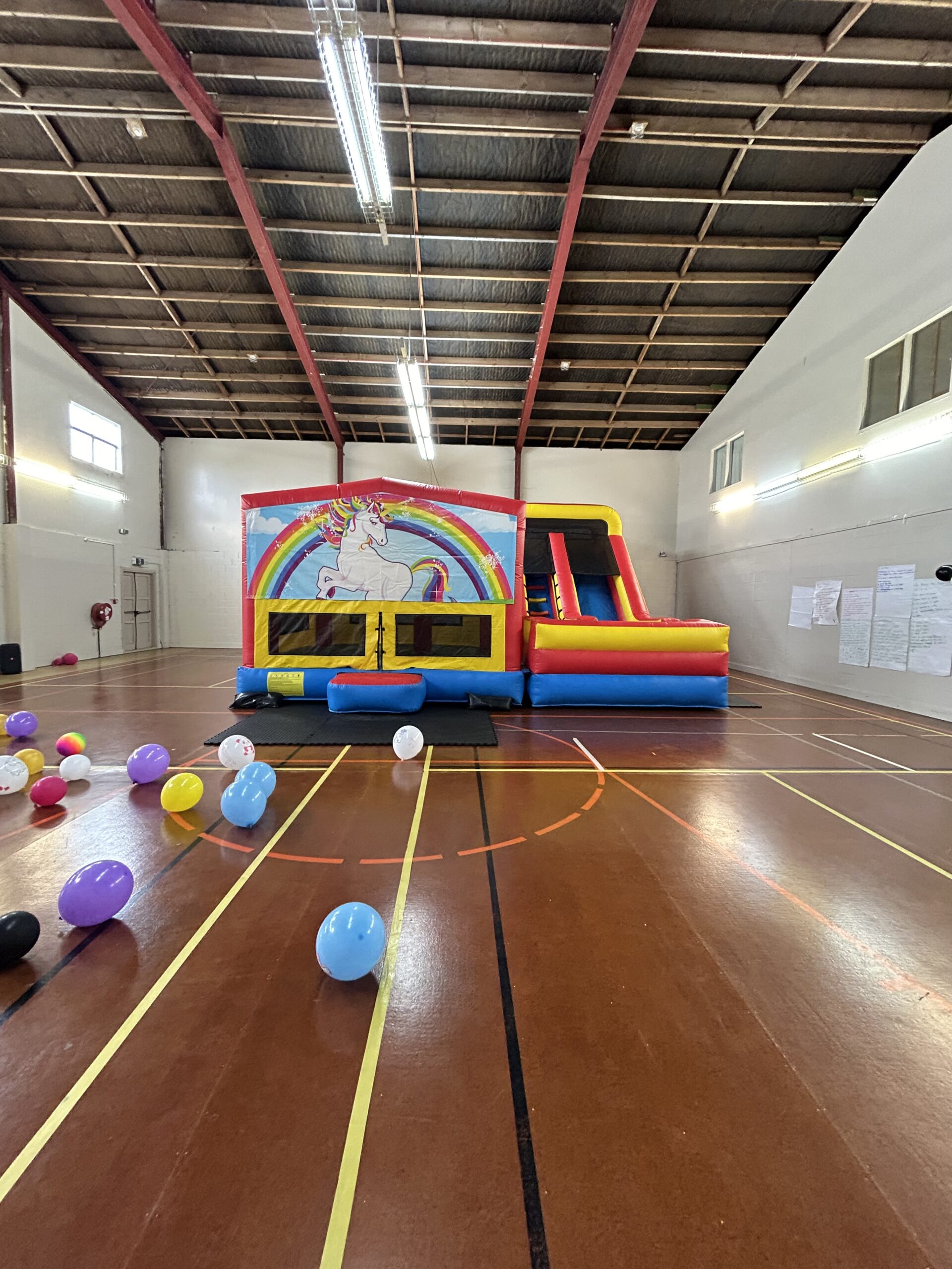 Open sports hall with metal roof structure, bouncy castle, and scattered balloons
