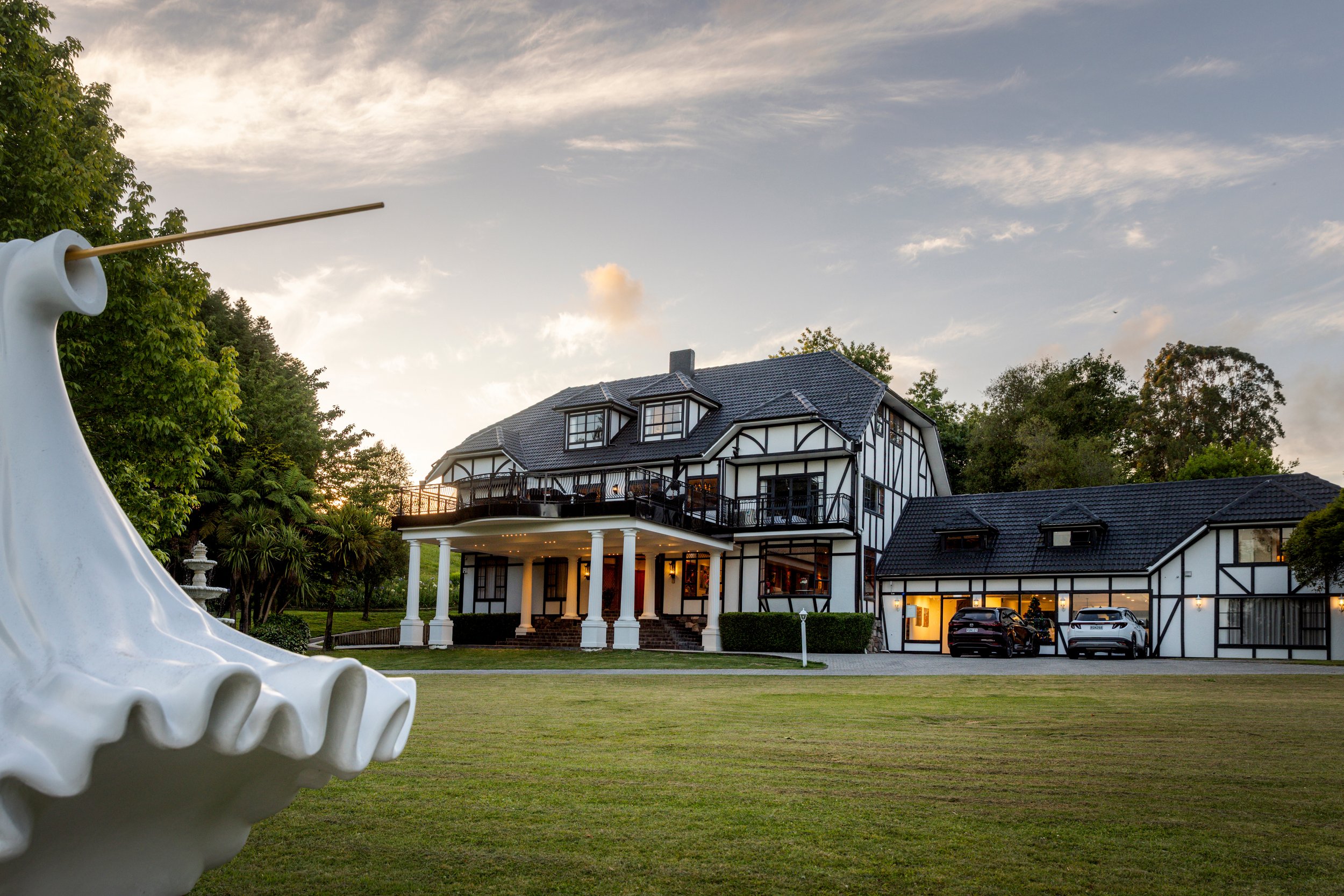 Tudor-style manor house and grounds at dusk with sculpture in foreground