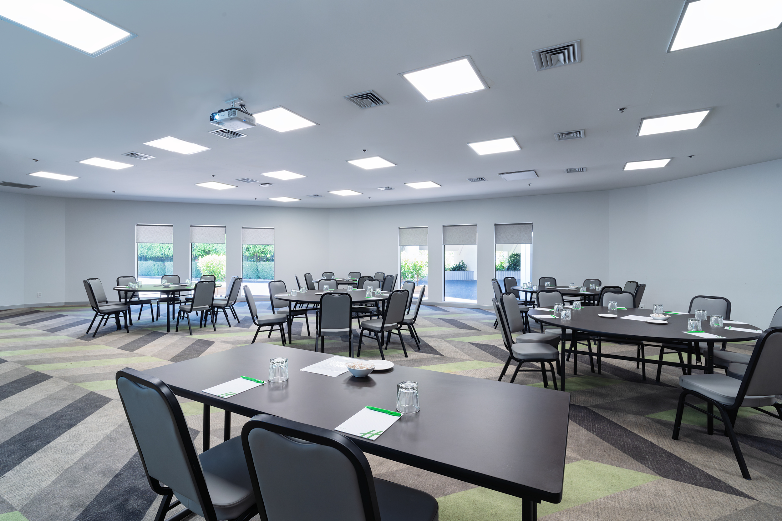 Neutral function room with round and rectangular tables, patterned floor, and row of windows