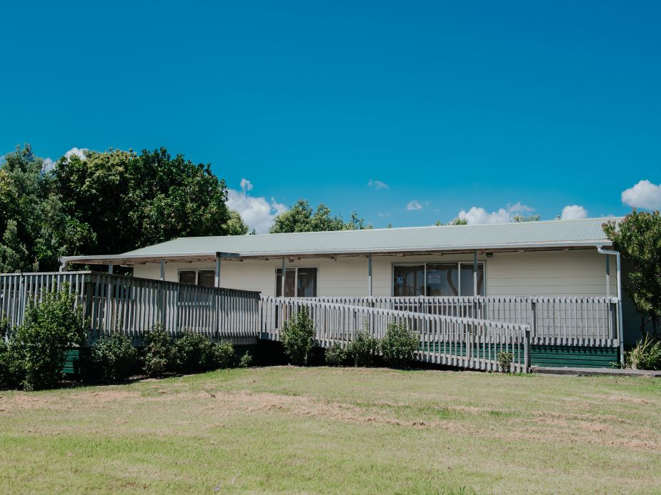 Single-storey weatherboard hall with veranda and grass lawn