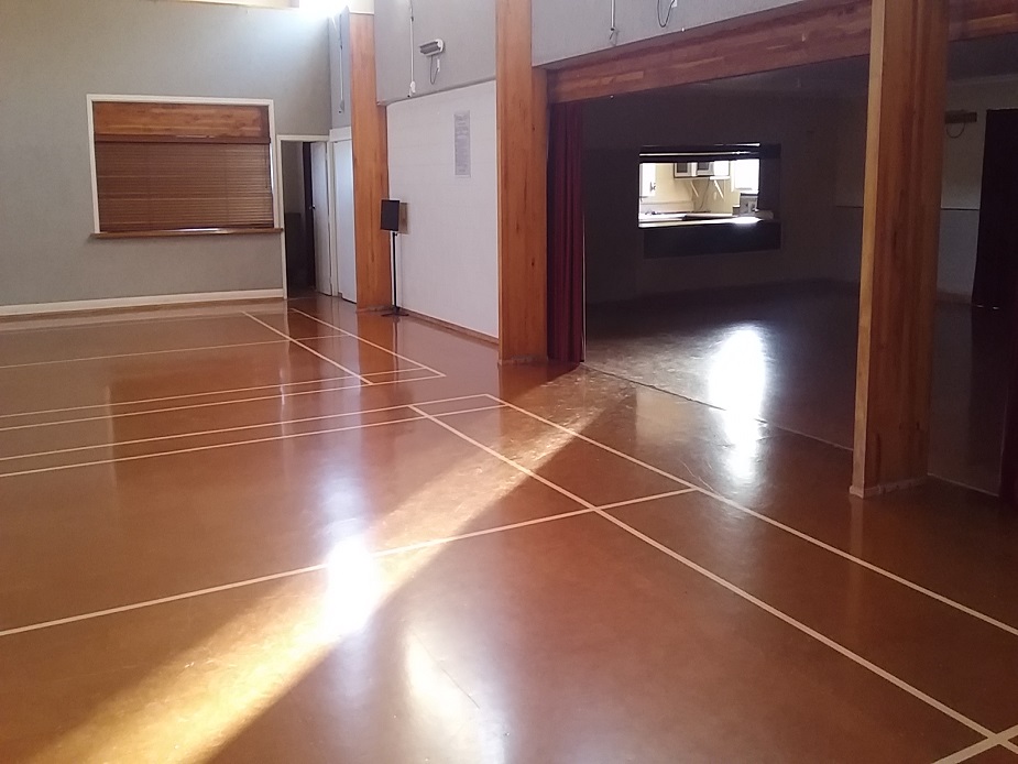 Empty polished brown-tiled hall with timber posts and a servery hatch, high ceiling