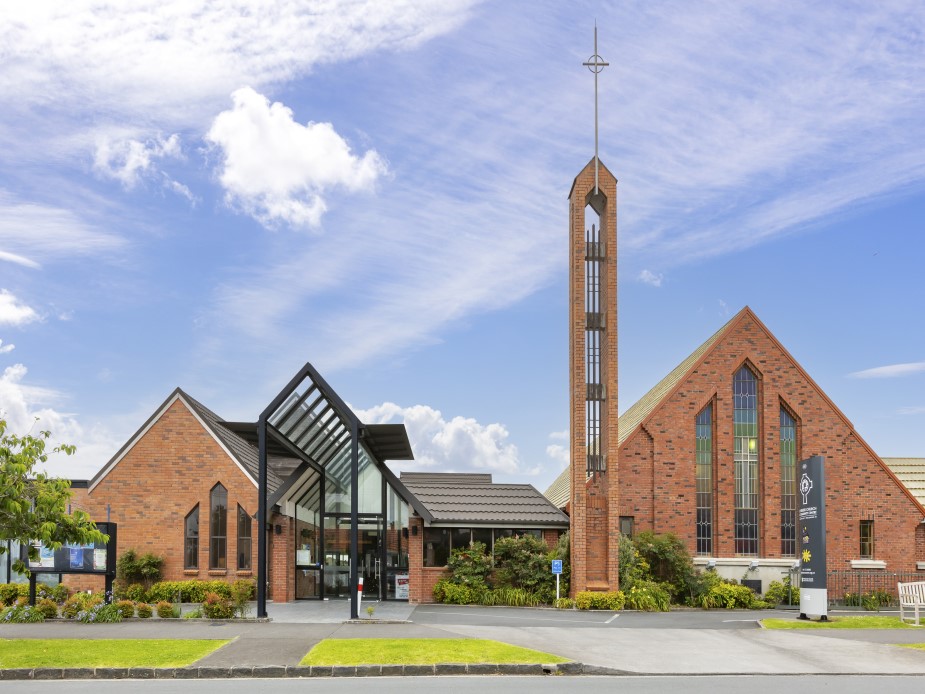 Red brick church complex with tall open-frame spire, pointed windows, and glass entry canopy