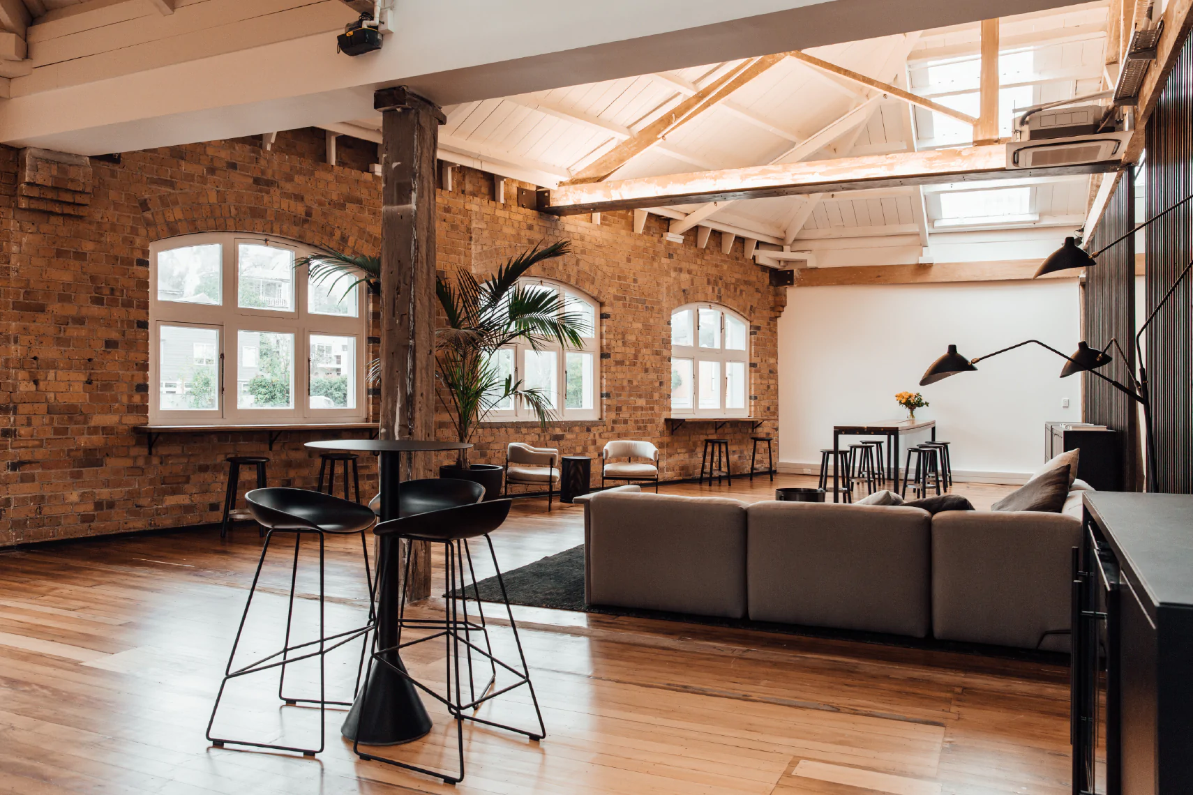 Brick-walled loft interior with exposed timber trusses, timber floor, bar tables and lounge seating