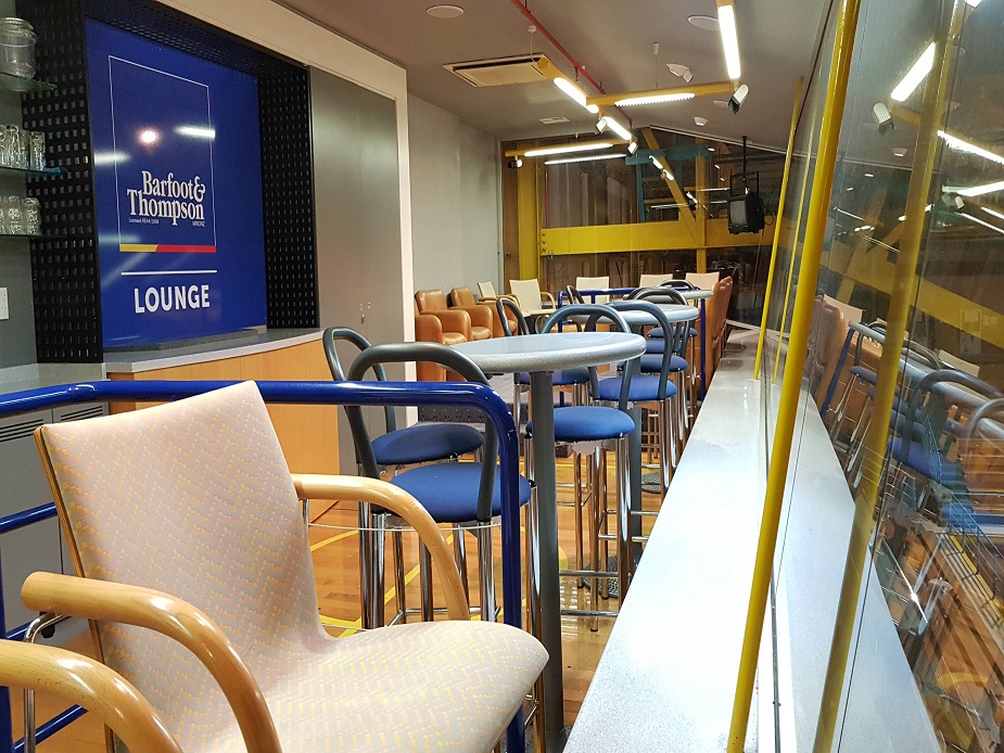 Lounge area overlooking an indoor sports court, with bar-height tables and mismatched chairs