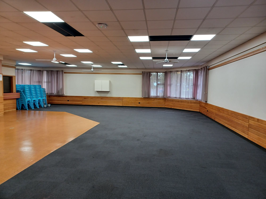 Large empty hall with carpet and timber-look floor, wooden wall panels and ceiling fans
