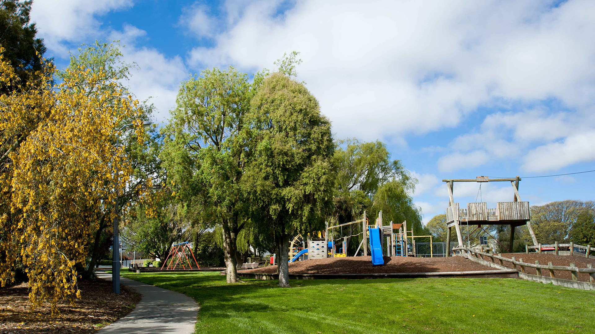 Park with playground equipment and mature trees under blue sky