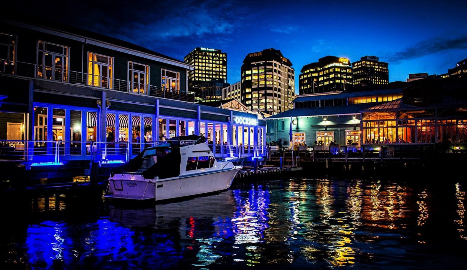 Dockside and city waterfront at night with blue lighting and a moored boat