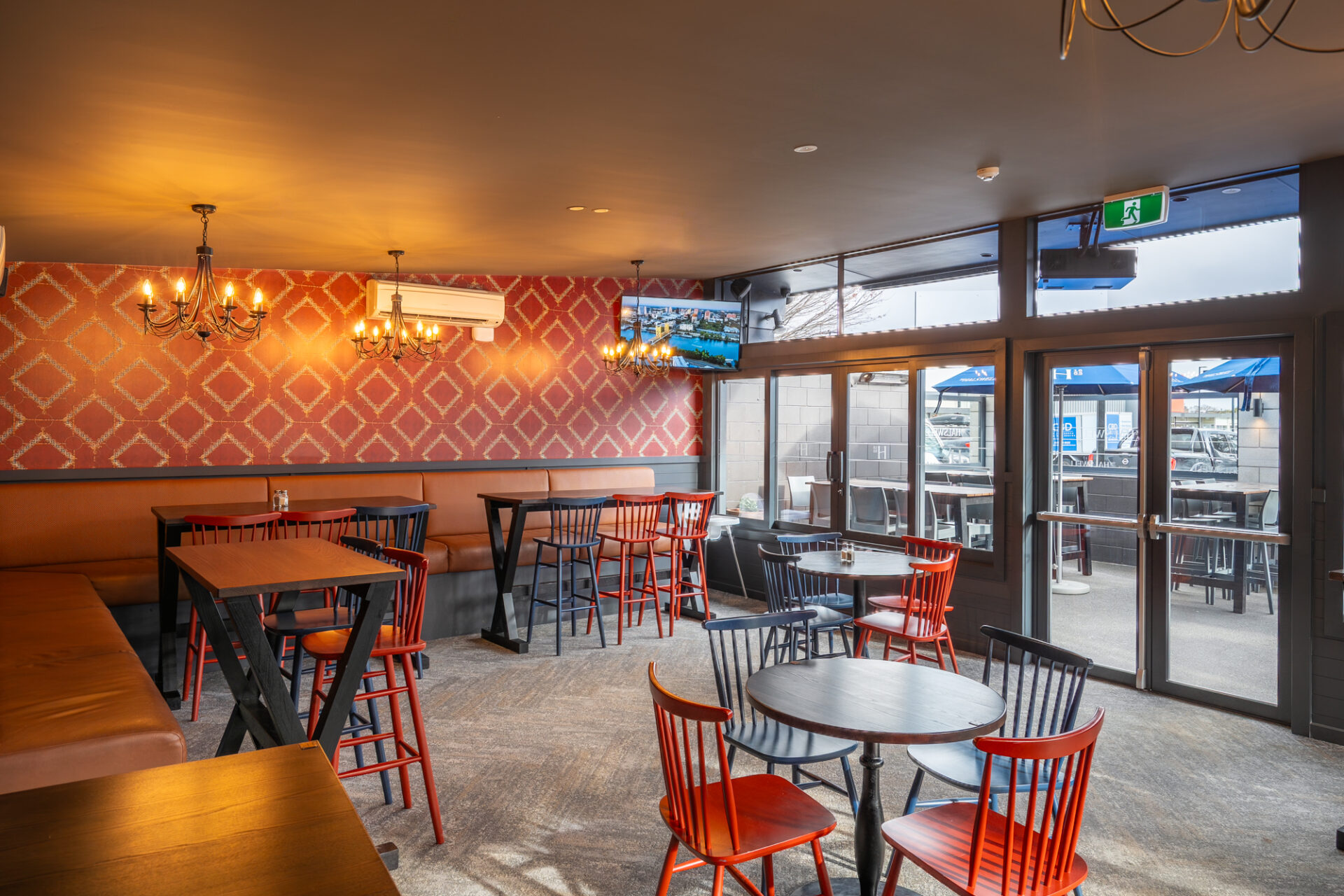 Bar dining room with red patterned wallpaper, leather booths and chandelier
