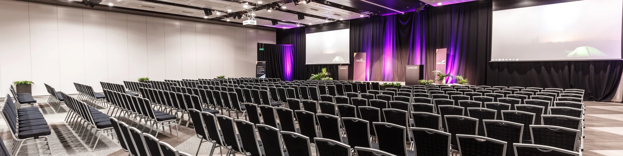 Conference hall set with rows of seats and projector screen on stage