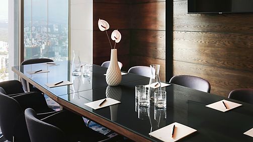 Dark-toned boardroom with polished table, upholstered chairs, and floor-to-ceiling city-view window