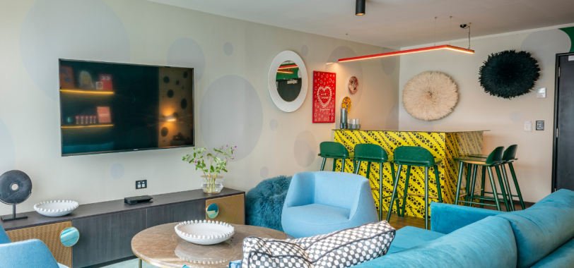 Colourful lounge area with blue sofa, yellow bar, green bar stools, and eclectic wall art