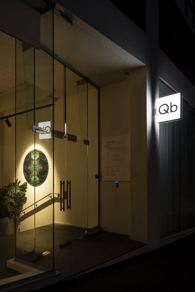 Illuminated glass entry at night with Qb signage on dark building facade