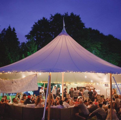 Marquee lit at night with guests seated inside under tall pole tent