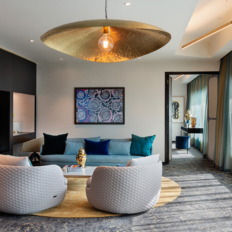 Dramatic hotel suite lounge with large gold pendant, teal sofa, patterned artwork, and rich textiles