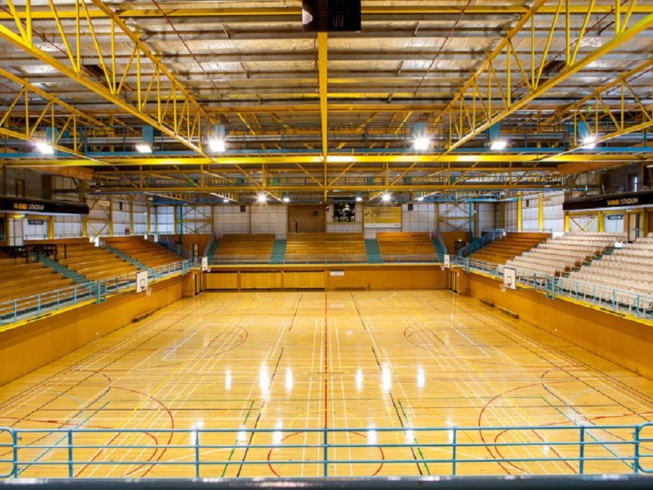 Large indoor sports arena with a timber court floor, tiered seating, and overhead truss structure