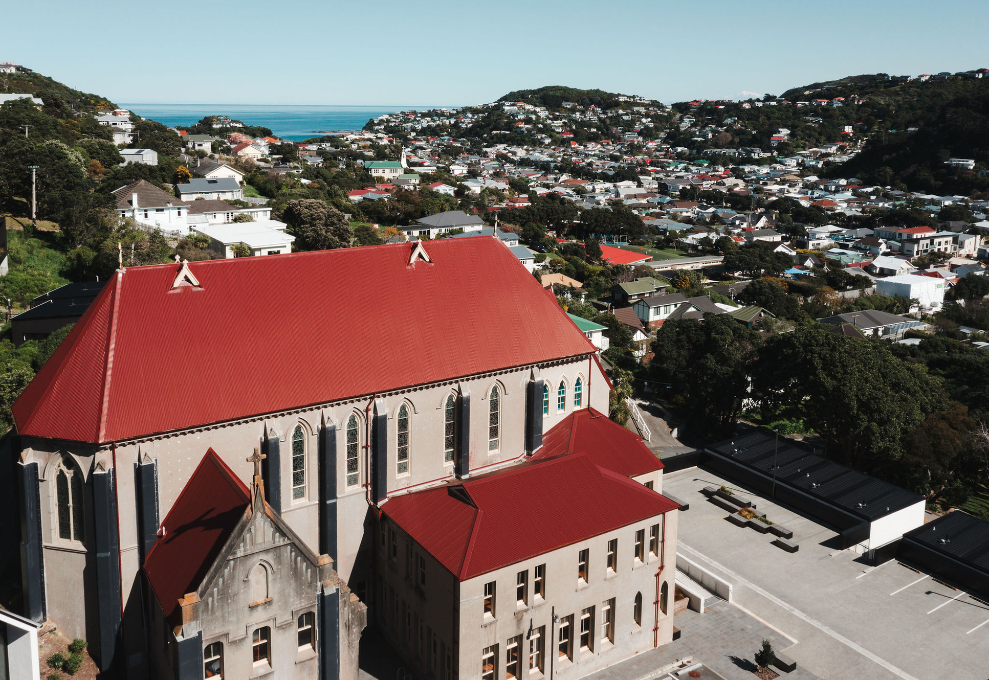 Wide aerial view of Gothic stone chapel with red roof and surrounding suburb