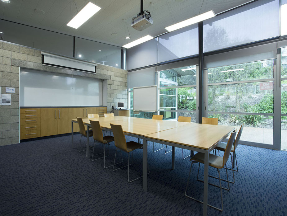 Meeting room with long table, chairs, projector screen, and garden view