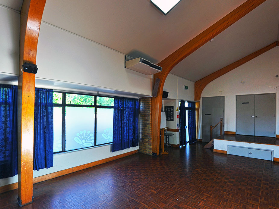 Main hall with timber arch columns, parquet floor and curtained windows